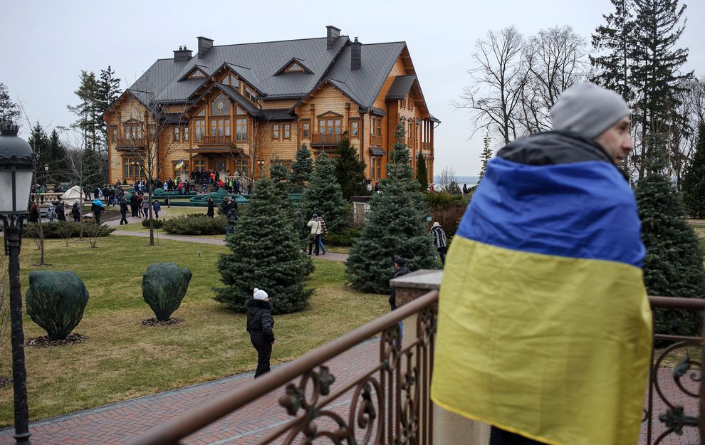 总统亚努科维奇位在郊外的府邸受到层层戒护，有一名乌克兰男子披着国旗站在屋外。摄影：ANDREW LUBIMOV