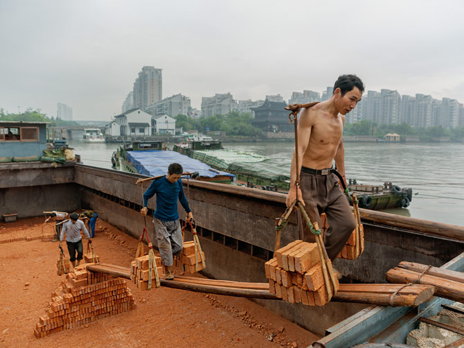 杭州的北新桥码头上，每一名挑夫都担着约90公斤重的砖块。挑夫一词的由来，是因为他们用手工制的竹扁担挑运货物。在运河沿岸的大部分地区，人力已被吊车和卡车取代。