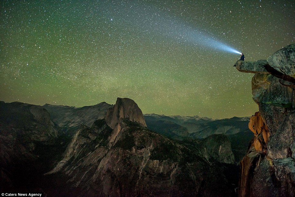 一名观星者坐在加州约塞米蒂国家公园的著名景点“冰川点”边缘处，头戴照明灯观赏美丽星空。