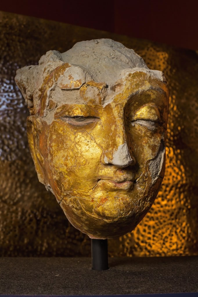 古老的面孔唤起了艾娜克遗址曾是中亚十字路口的过往；其中有镀金石膏的佛陀面孔，高20.3公分。 Photograph by Simon Norfolk
