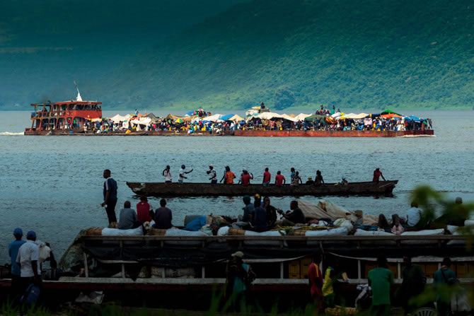 有宽敞寝室的公共运输船曾经往来于刚果河上，但刚果民主共和国的政府却任由这些船只荒废失修。现在河上运输主要靠驳船（上）与独木舟（中央）。 Photograph b