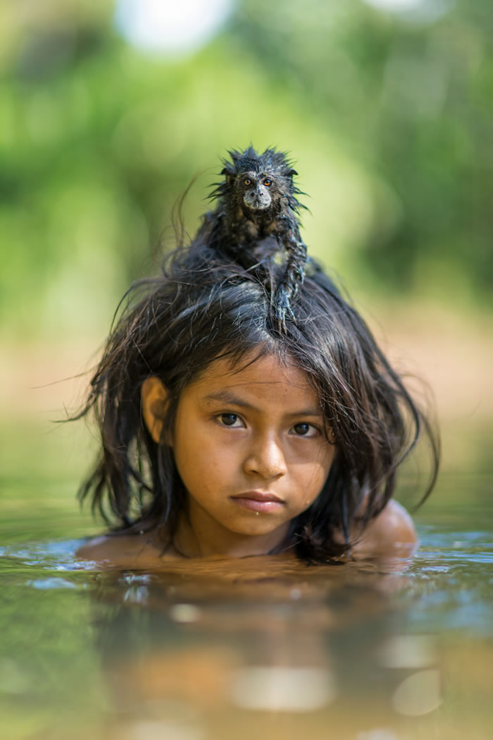 马奇健格族女孩尤伊娜．马美利亚．诺索德加在马努国家公园深处的尤米巴托河游泳，她养的黑褐獠狨紧紧抓着她。 Photograph by Charlie Hamilt