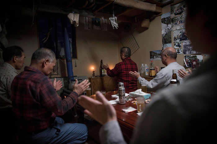 分配猎物后，小国町的猎人聚在佐藤队长的家里，开始仪式。远藤先生是群体中备受敬重的又鬼猎人，他以一颗熊的心脏与一瓶清酒来主持祈祷。 PHOTOGRAPH BY J