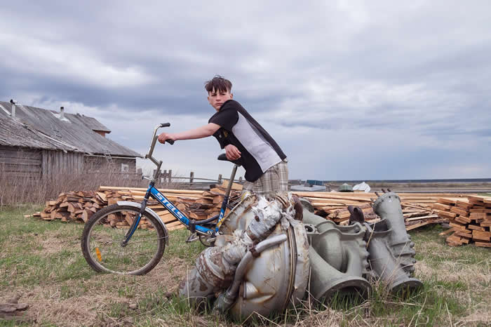 13岁的安东（Anton）站在俄罗斯北方道嘉屈莱村（Dolgoshchel’ye）的一块火箭零件旁边。北极圈下方约有10个聚落的居民会去捡拾太空垃圾，这个村子就