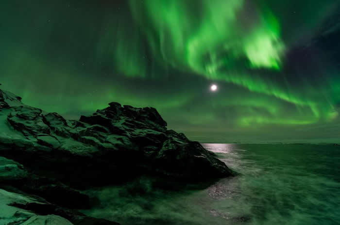 在挪威Laksefjorden地区，月色透过夜空中如帘幕般的极光闪耀着。 PHOTOGRAPH BY ERLEND HAARBERG, NATIONAL GEO
