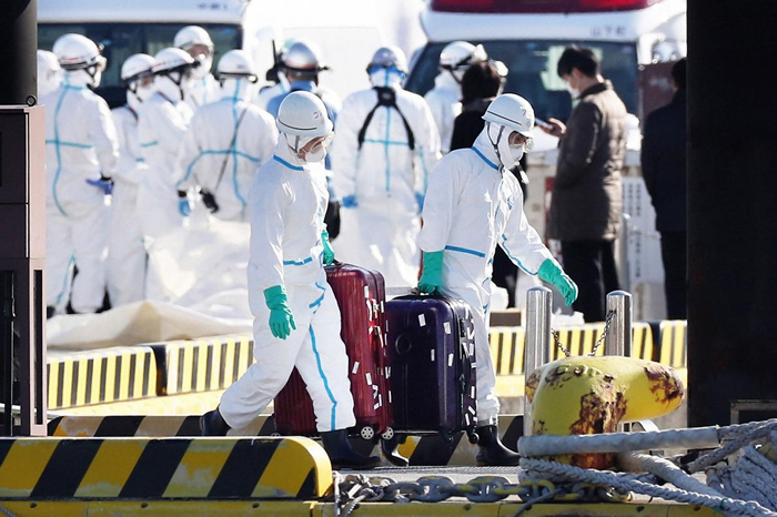 身着防护装备的卫生官员从停泊在日本横滨的钻石公主号游轮上带出行李箱，大众普遍认为这些行李箱的主人，就是验出冠状病毒阳性后从船上撤离送医的乘客。 PHOTOGRA