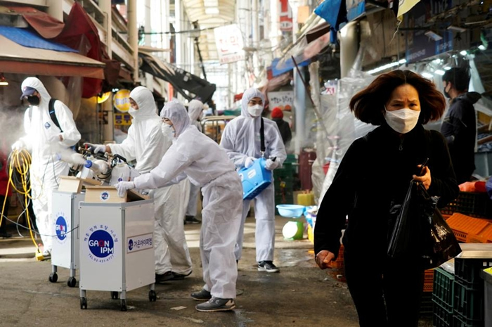 2020年2月26日，消毒公司的员工在帮南韩首尔一处传统市场消毒，旁边一名女性戴着口罩，以免感染新型冠状病毒。 PHOTOGRAPH BY KIM HONG-J