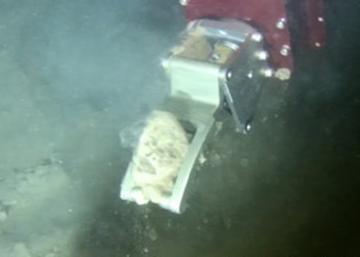 潜水器以机械手在深渊海底取样。