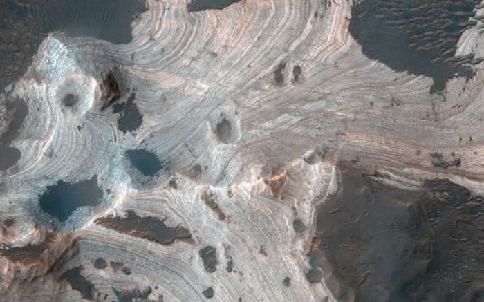 这张照片是由美国宇航局火星勘测轨道飞行器（MRO）机载高分辨率科学实验成像相机（HiRISE）拍摄的，呈现出直径140公里的霍尔顿陨坑中存在漩涡层状砂岩。